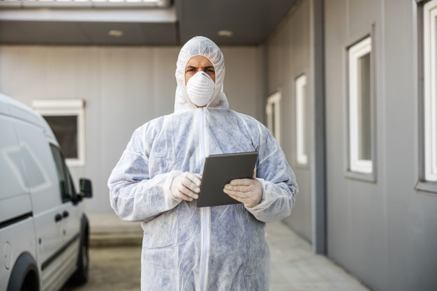 man-virus-protective-suit-mask-looking-typing-tablet-disinfecting-buildings-coronavirus-with-sprayer-epidemic_232070-7919